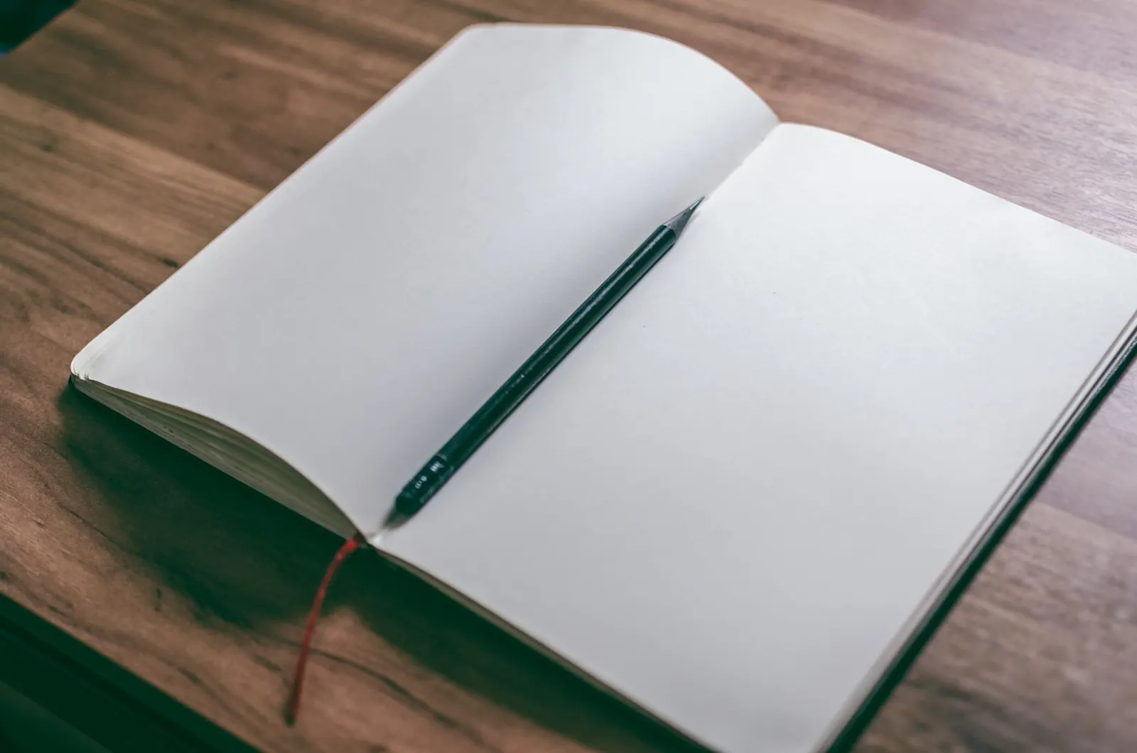 Open sketchbook and pencil on wooden desk, perfect for creativity and design concepts.